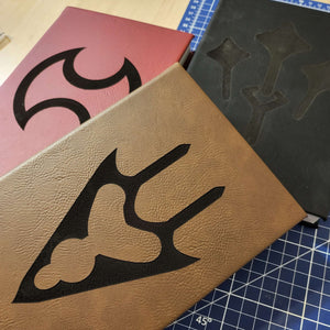 Three leather journals with cut-out designs on a cutting mat.