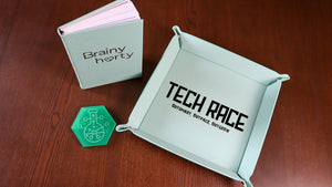 Sea green dice tray with 'Tech Race' branding, next to custom coasters and a an engraved leather journal.
